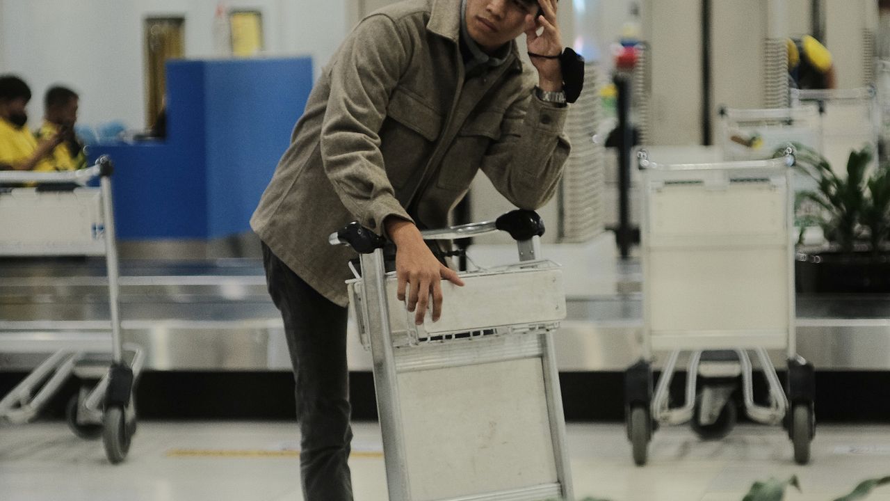 A traveller standing beside luggage carts in an airport arrivals hall