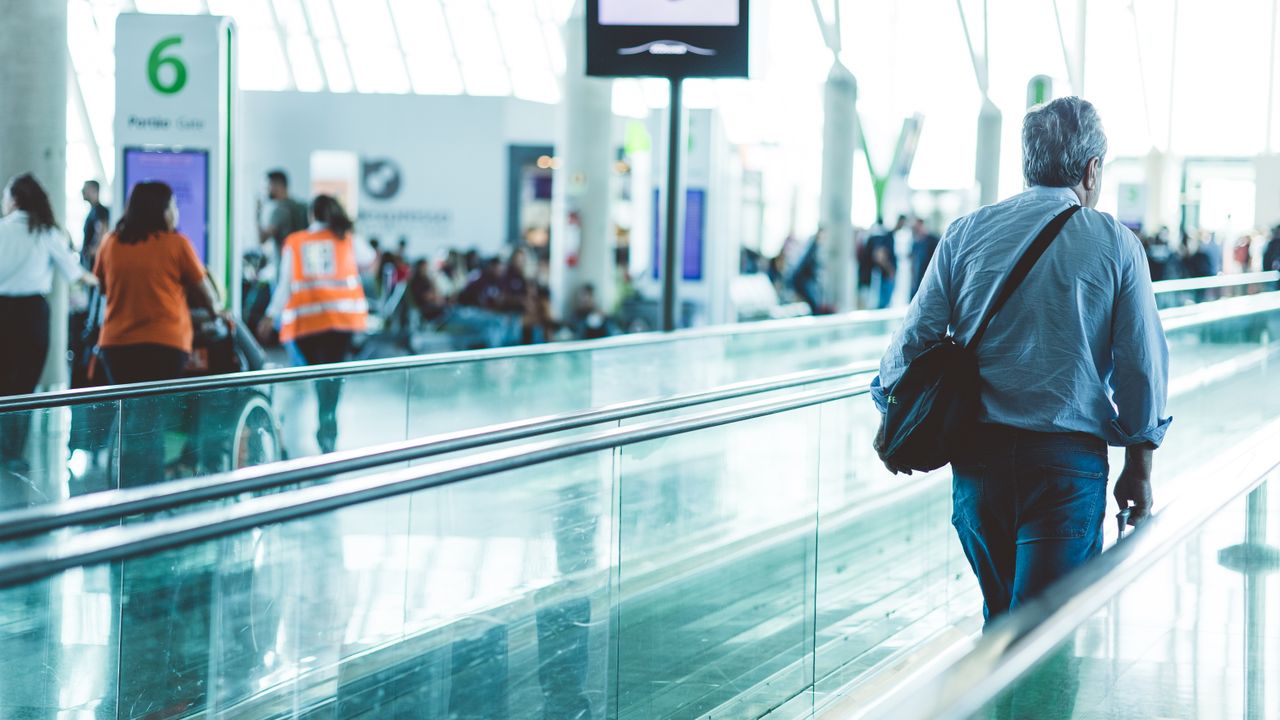 A traveller walking along an airport moving walkway beneath lit signage