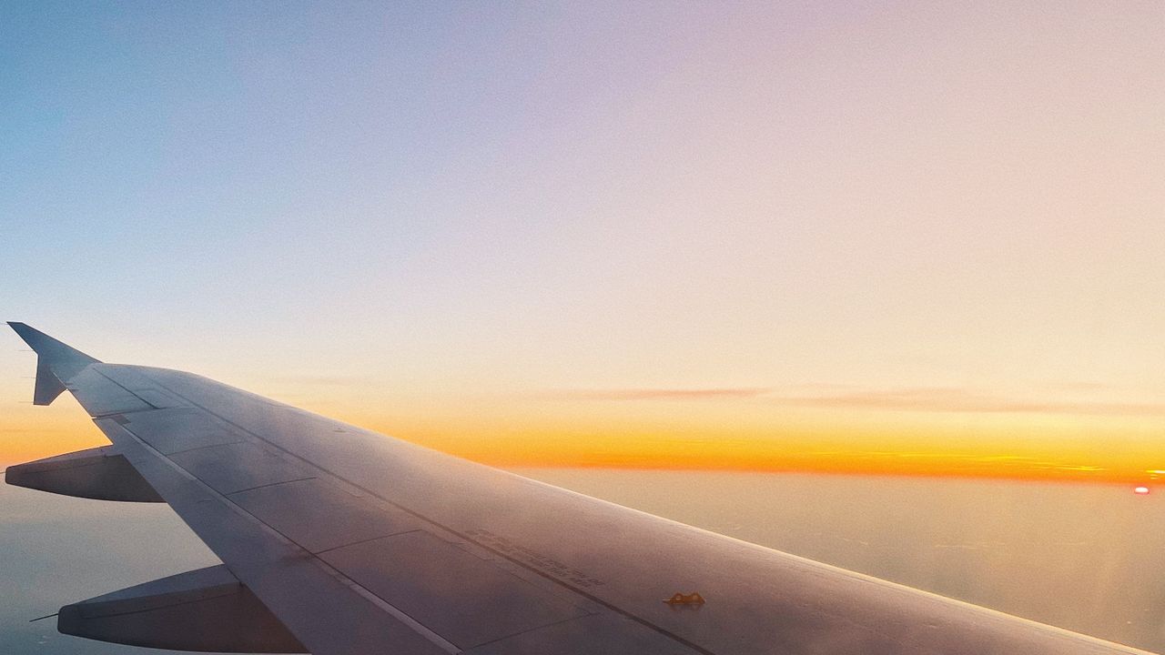 An aircraft wing above a sunset gradient seen through a cabin window